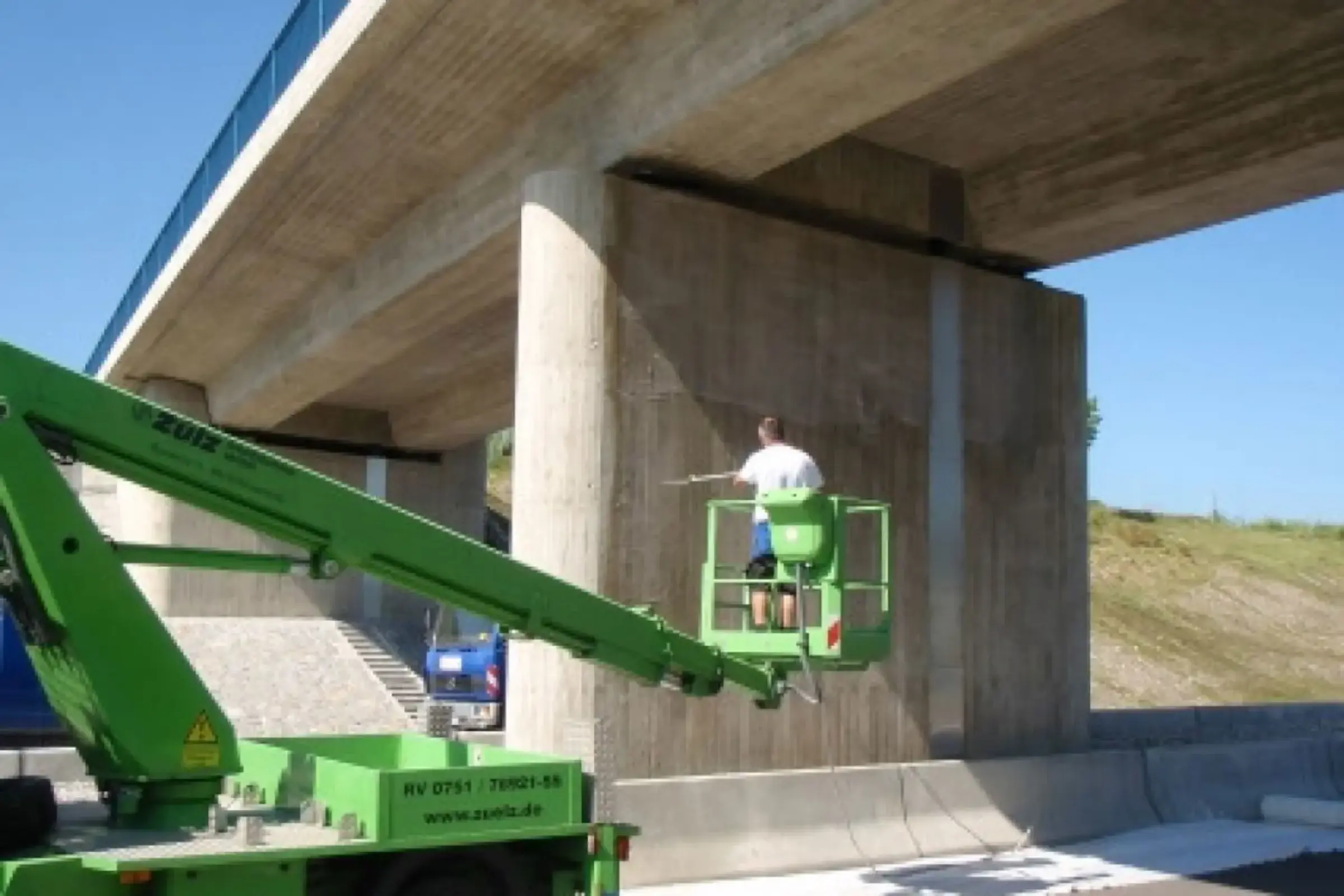 Un ouvrier spécialisé applique l'hydrofuge en profondeur sur un mur en béton à l'aide d'une grue.