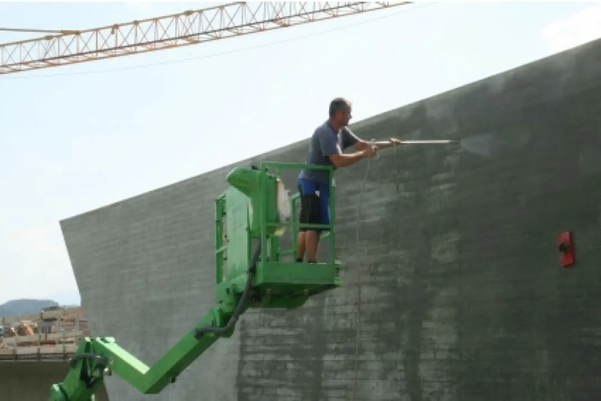 Un ouvrier spécialisé applique l'hydrofuge en profondeur sur un mur en béton à l'aide d'une grue.