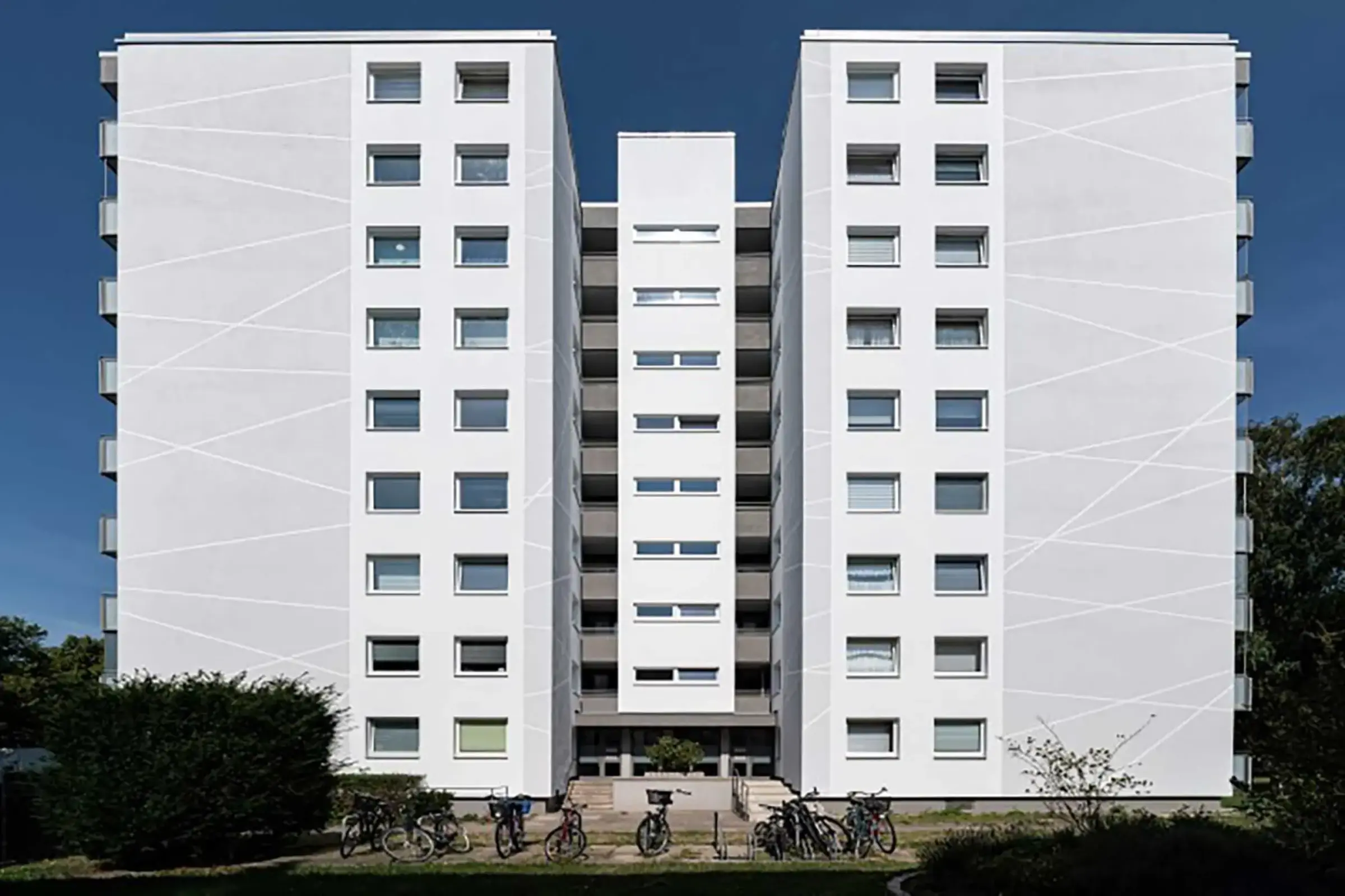 Saniertes Hochhaus mit weissem Putz und grauen Balkonen von vorne