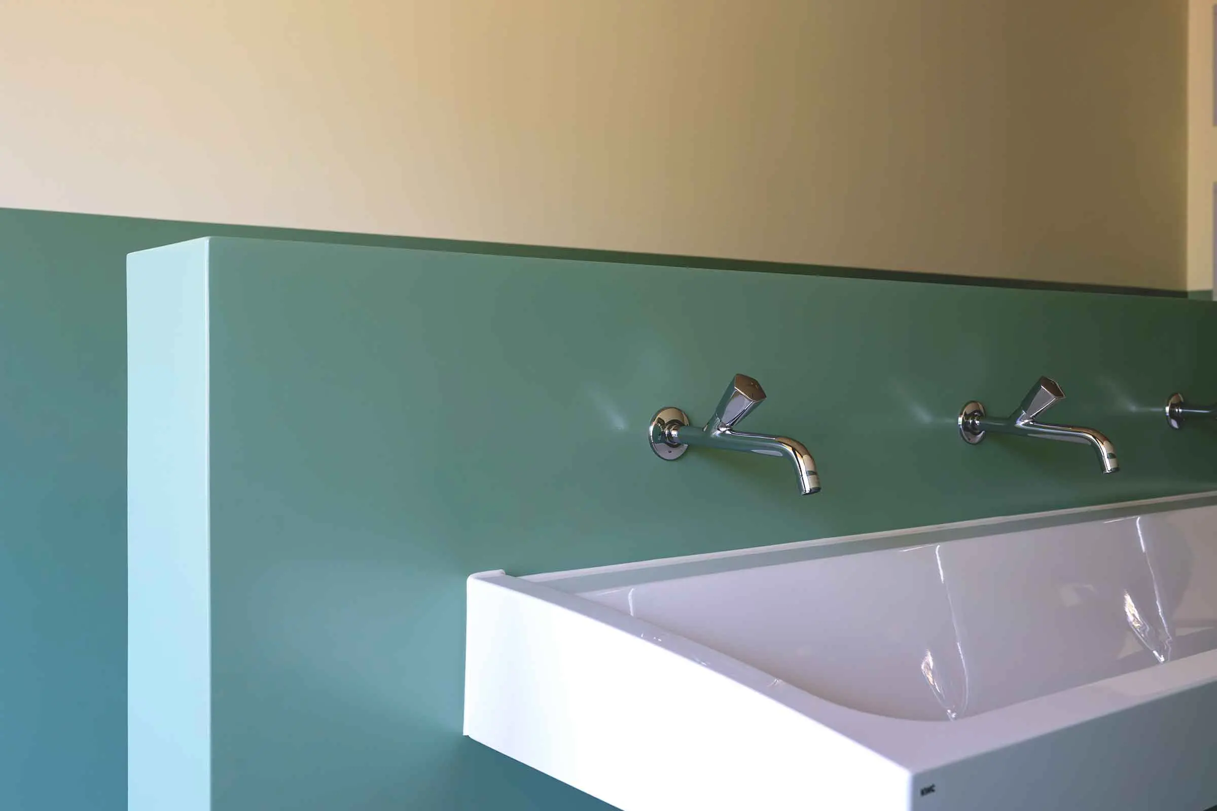 Salle d'eau avec lavabos blancs et revêtement mural vert sans joints