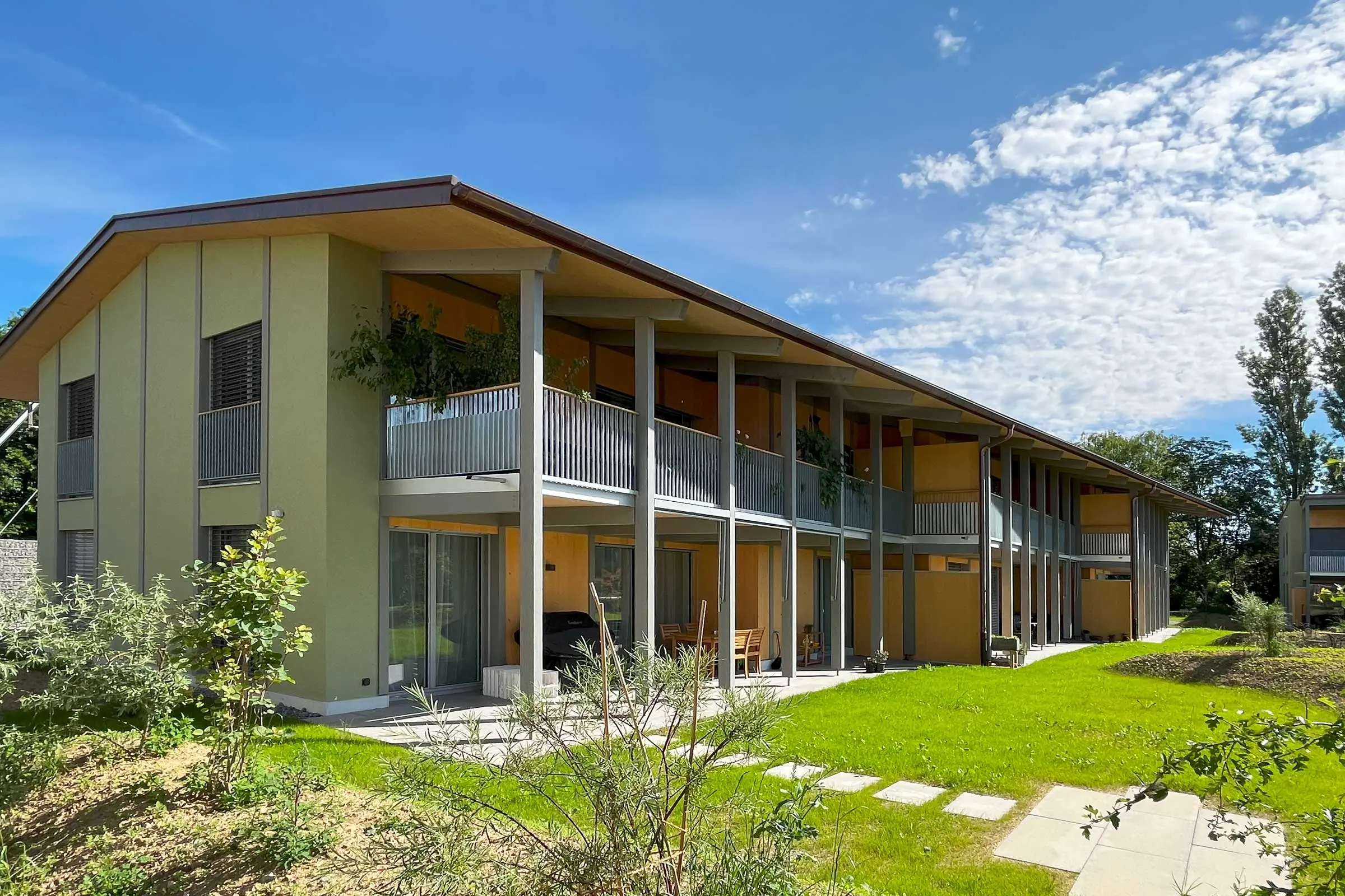 Ansicht Mehrfamilienhaus mit gelbem Fassadenputz und Balkonen an der Längsseite