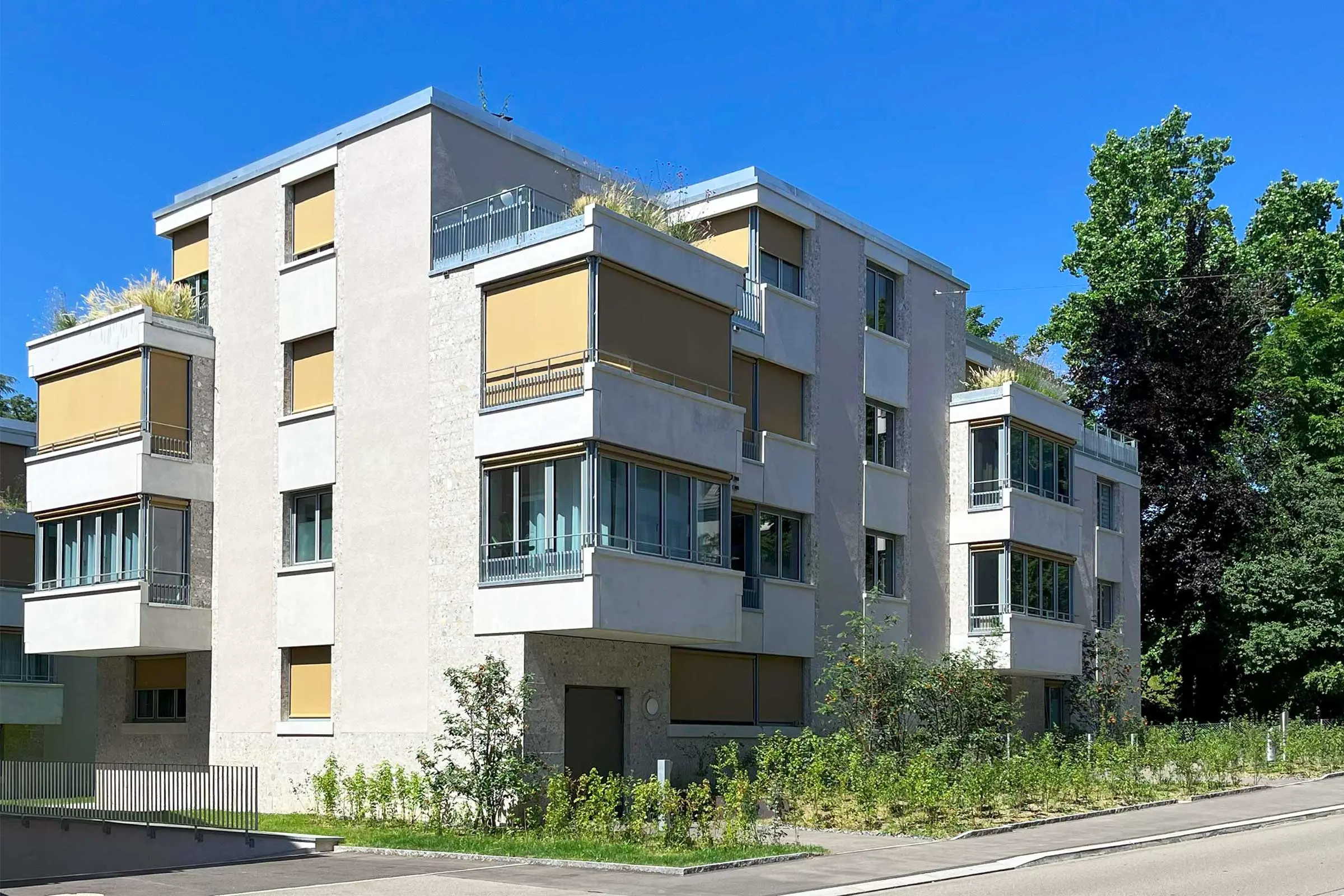 Gesamtansicht Mehrfamilienhaus mit beigem Fassadenputz und braunen Rollos