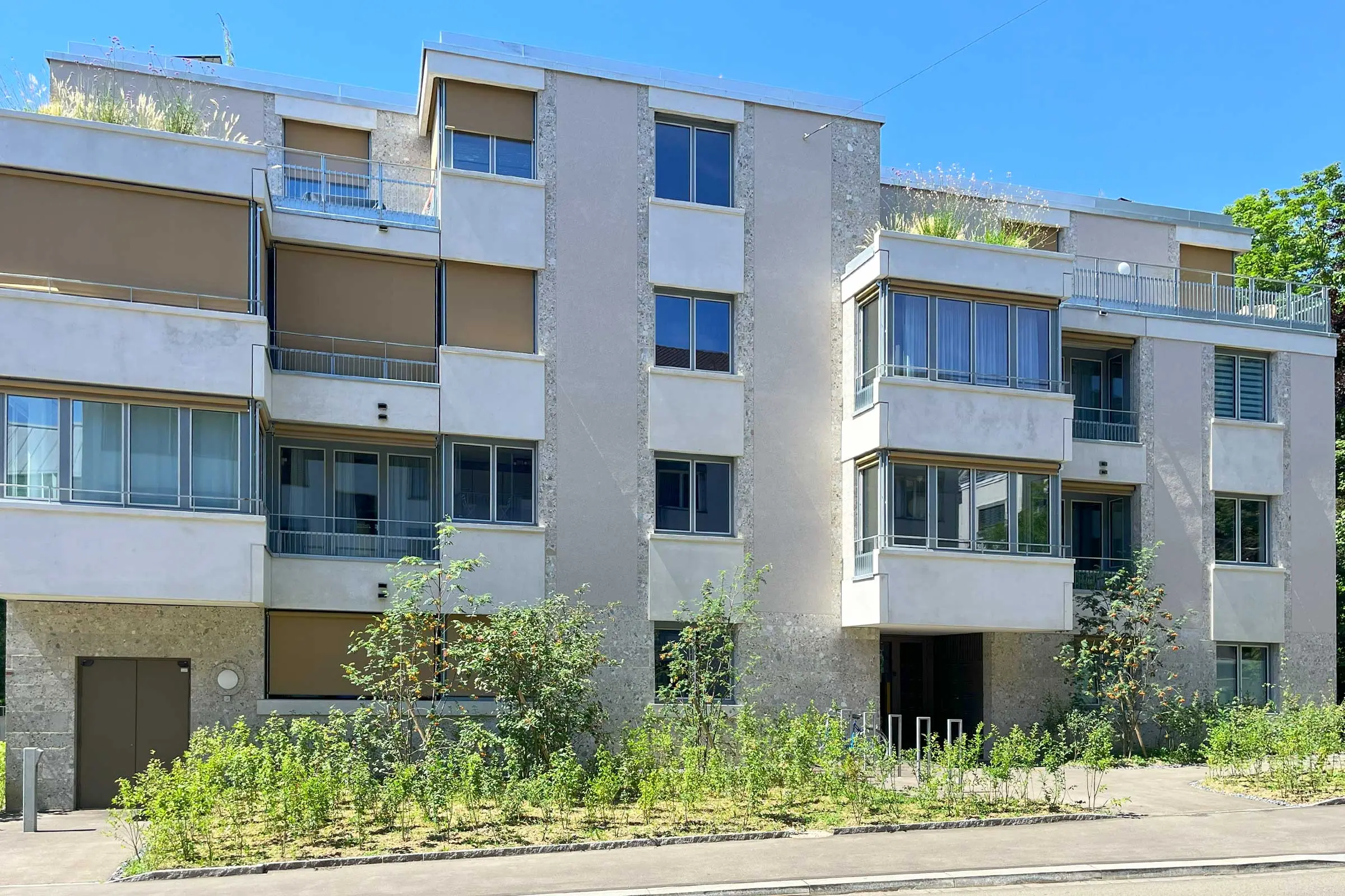 Frontansicht Mehrfamilienhaus mit beigem Fassadenputz und braunen Rollos