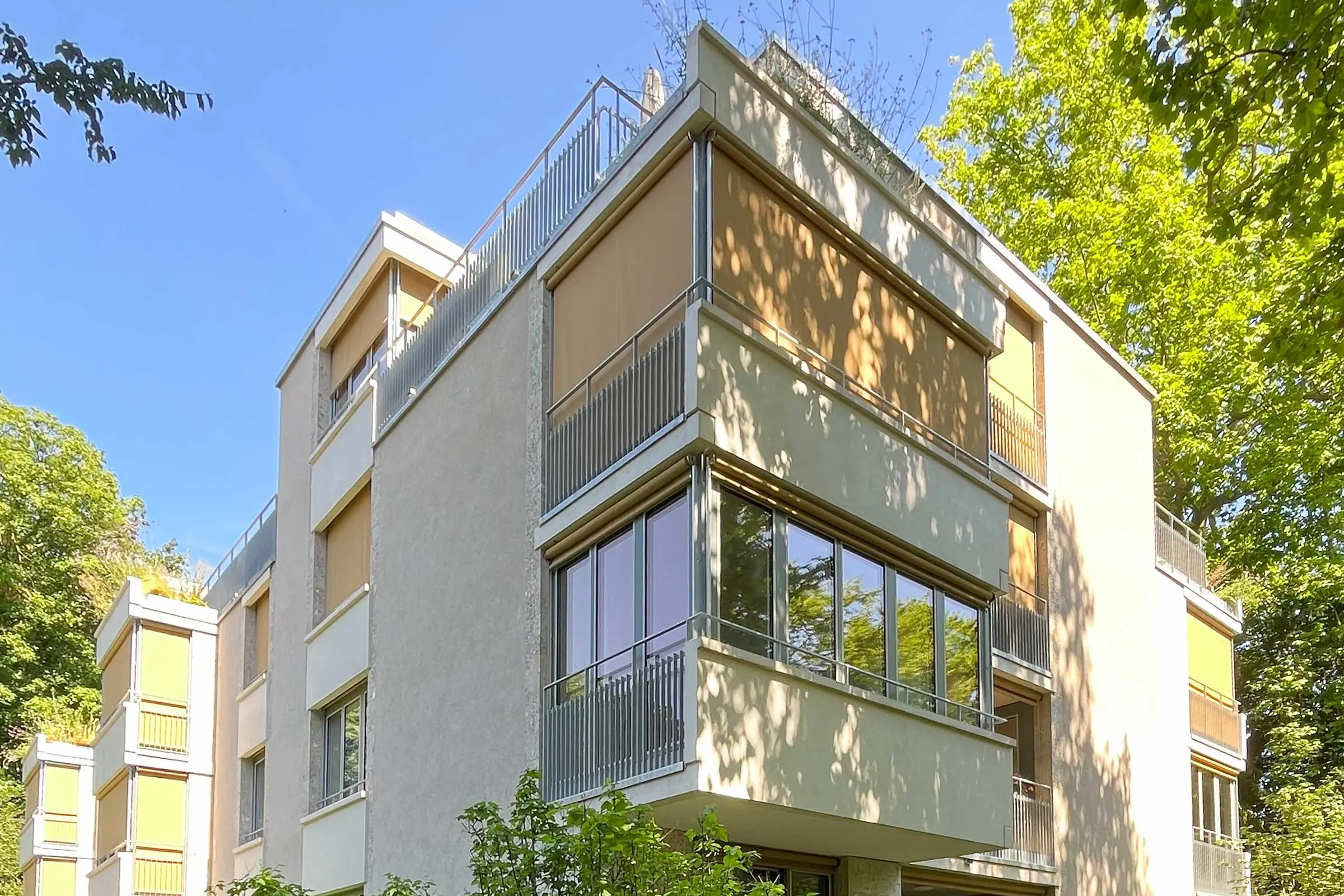 Eckansicht Mehrfamilienhaus mit beigem Fassadenputz und braunen Rollos