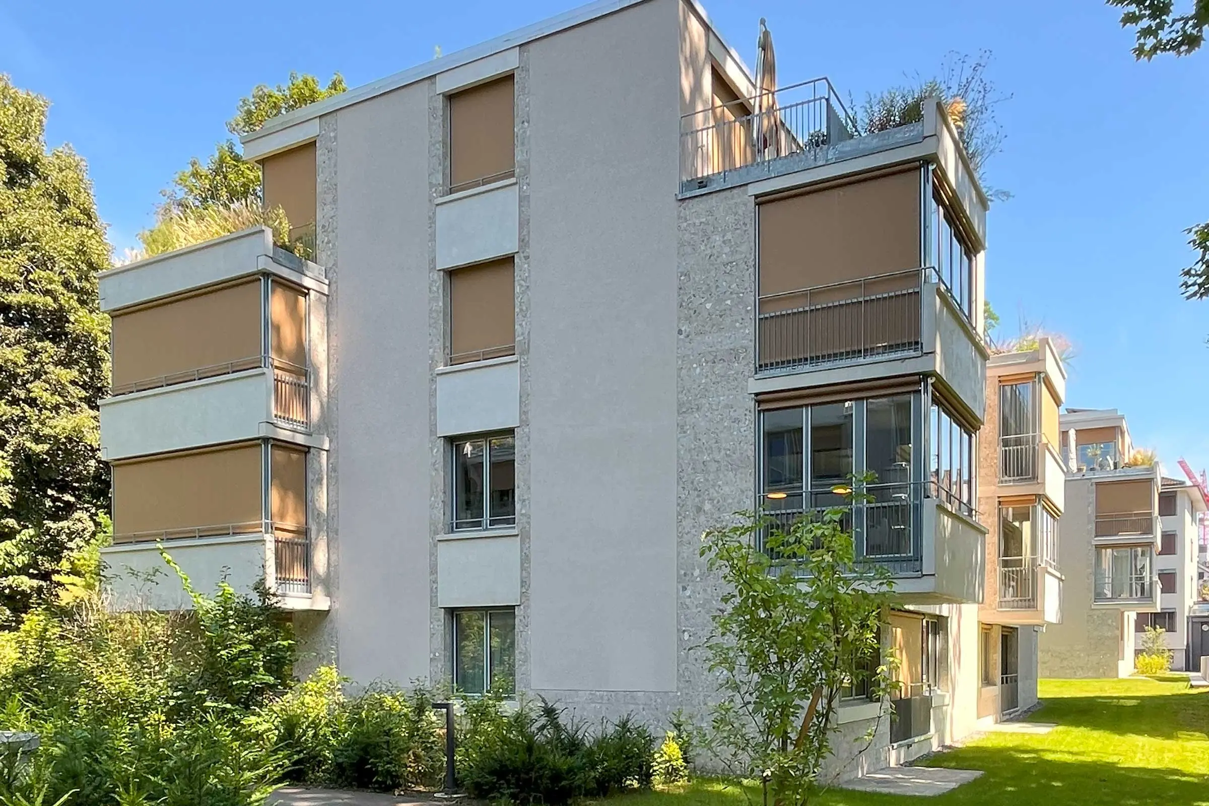 Mehrfamilienhaus in mit beigem Fassadenputz und braunen Rollos