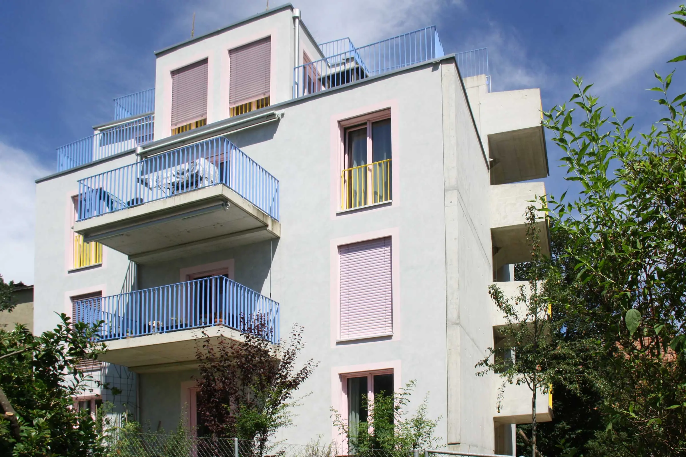 Mehrfamilienhaus aus Sichtbeton mit rosa Fensterumrandung mit Balkonen