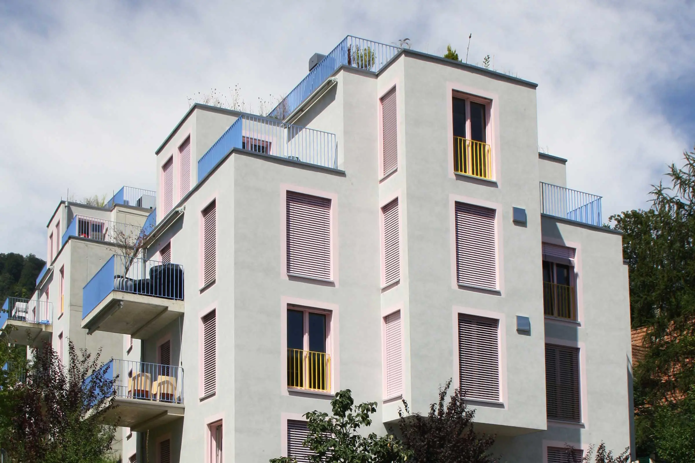 Mehrfamilienhaus aus Sichtbeton mit rosa Fensterumrandung und blauen Balkonen