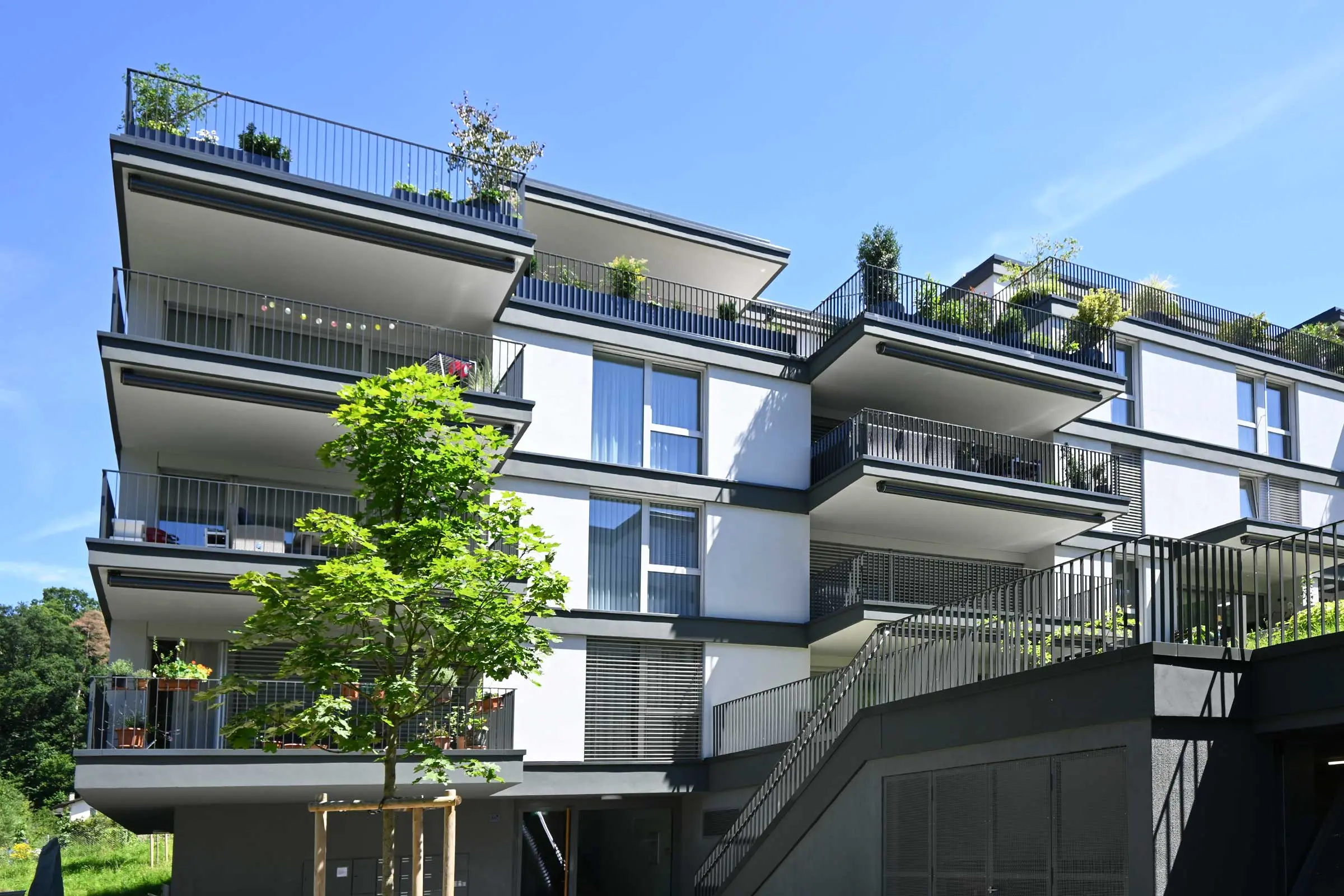 Mehrfamilienhaus mit heller Fassadenbeschichtung, Ansicht mit Balkonen von vorne