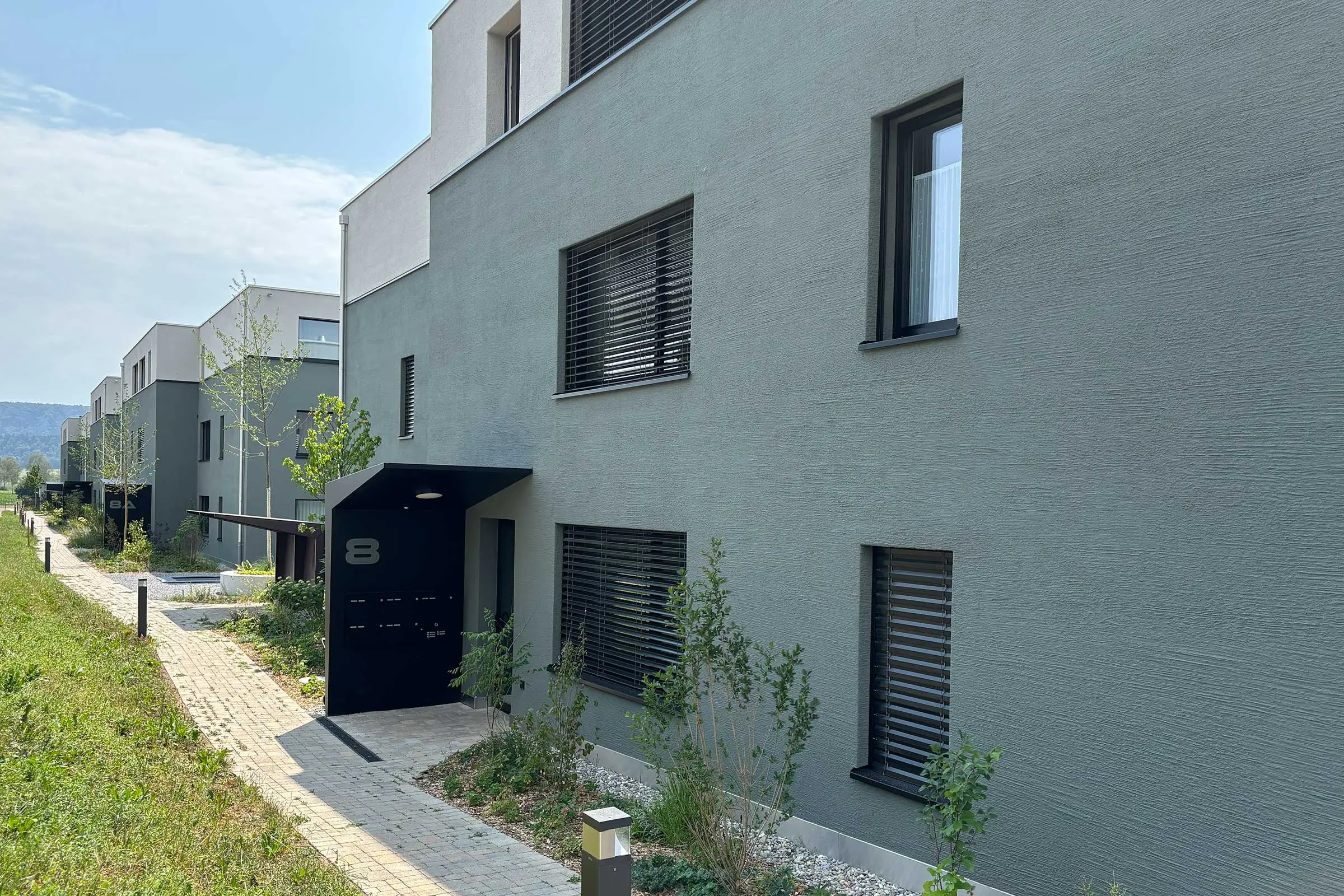 Moderne Mehrfamilienhäuser mit Flachdach und grüner Fassade unten und oben hell.