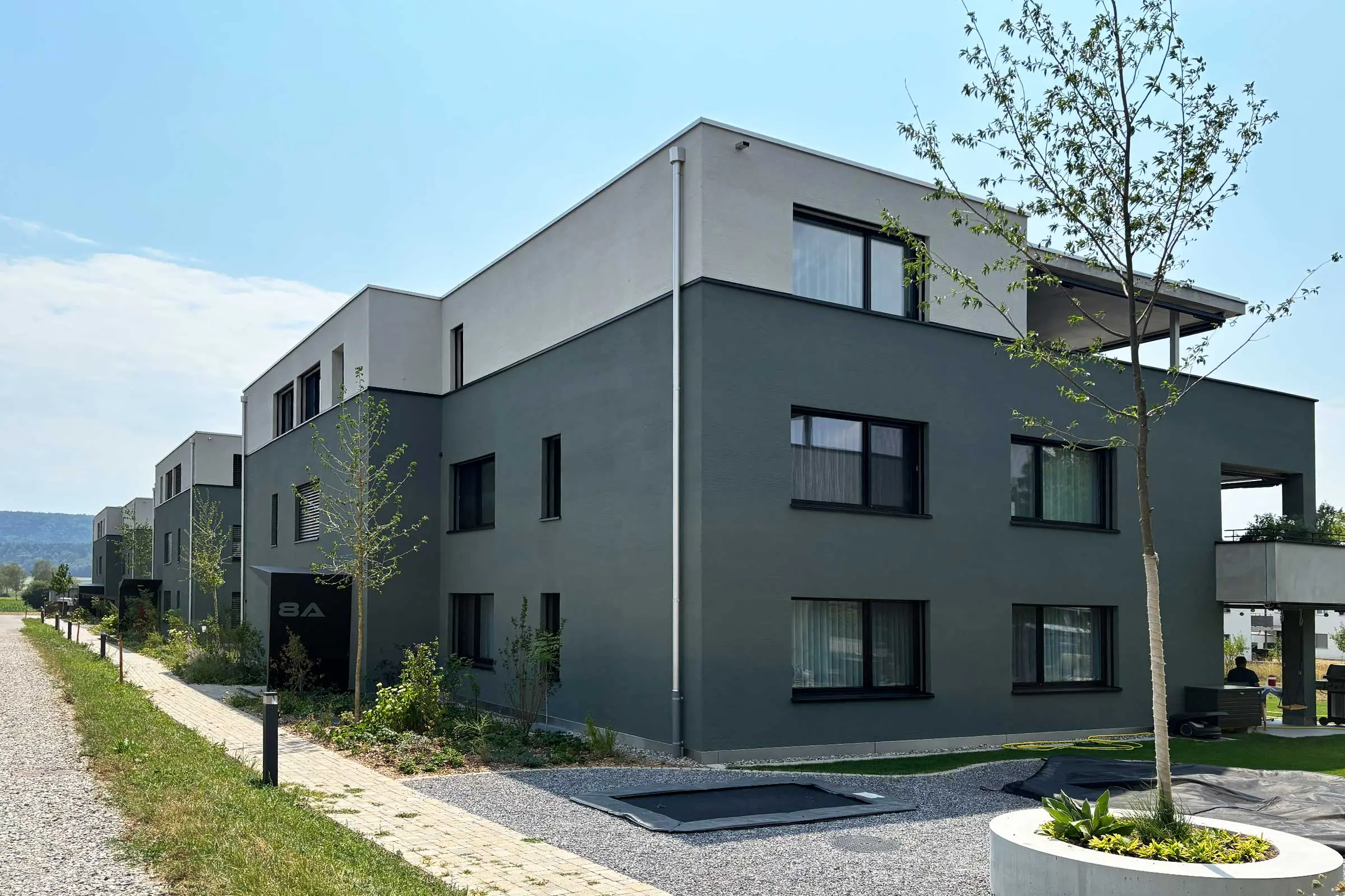 Moderne Mehrfamilienhäuser mit Flachdach und grüner Fassade unten und oben hell als Akzent