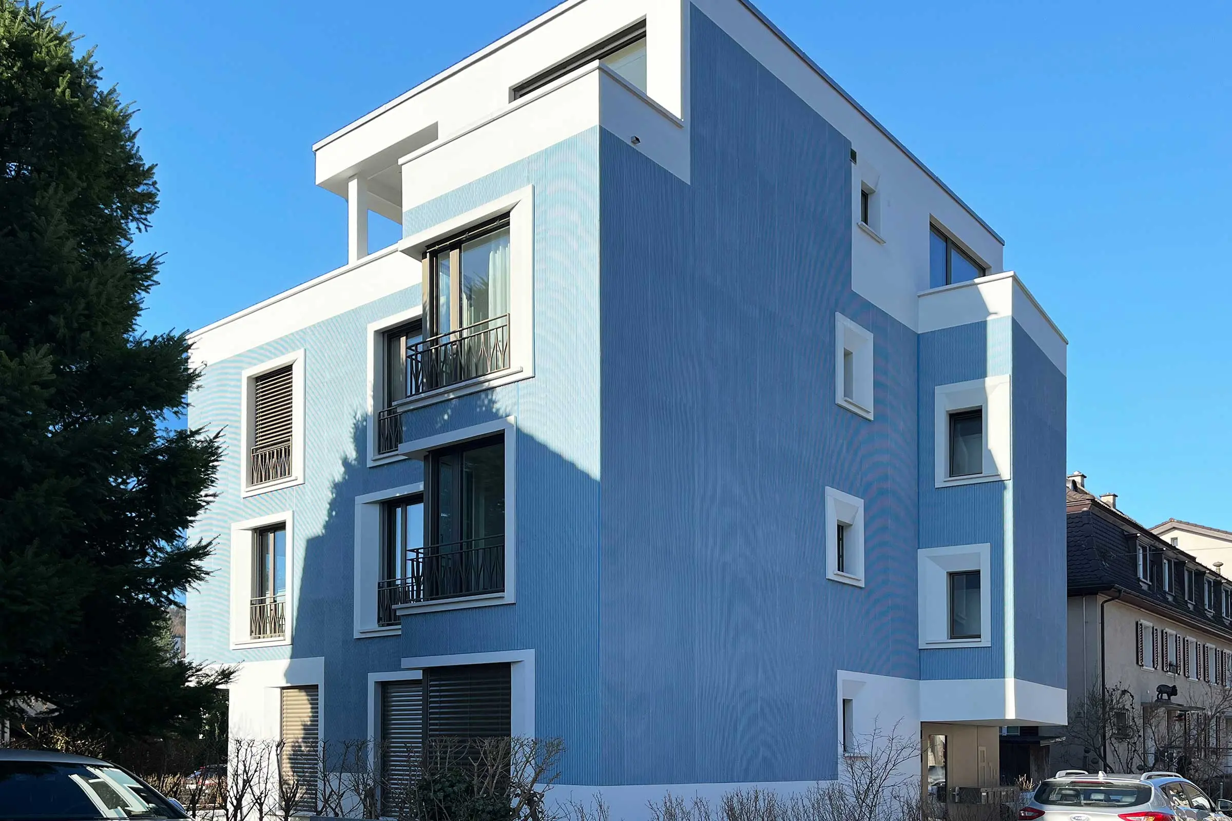 Mehrfamilienhaus mit blauer Putzfassade und weissen Fensterumrandungen