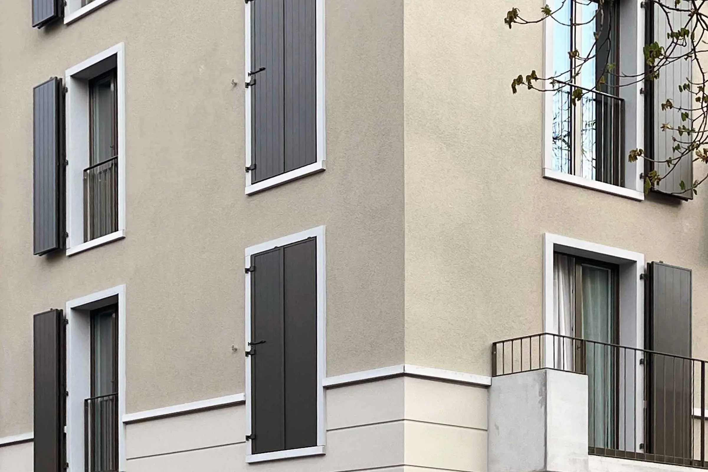 Eckansicht eines Mehrfamilienhauses mit hellbrauener Putzfassade und dunkelbraunen Fensterläden