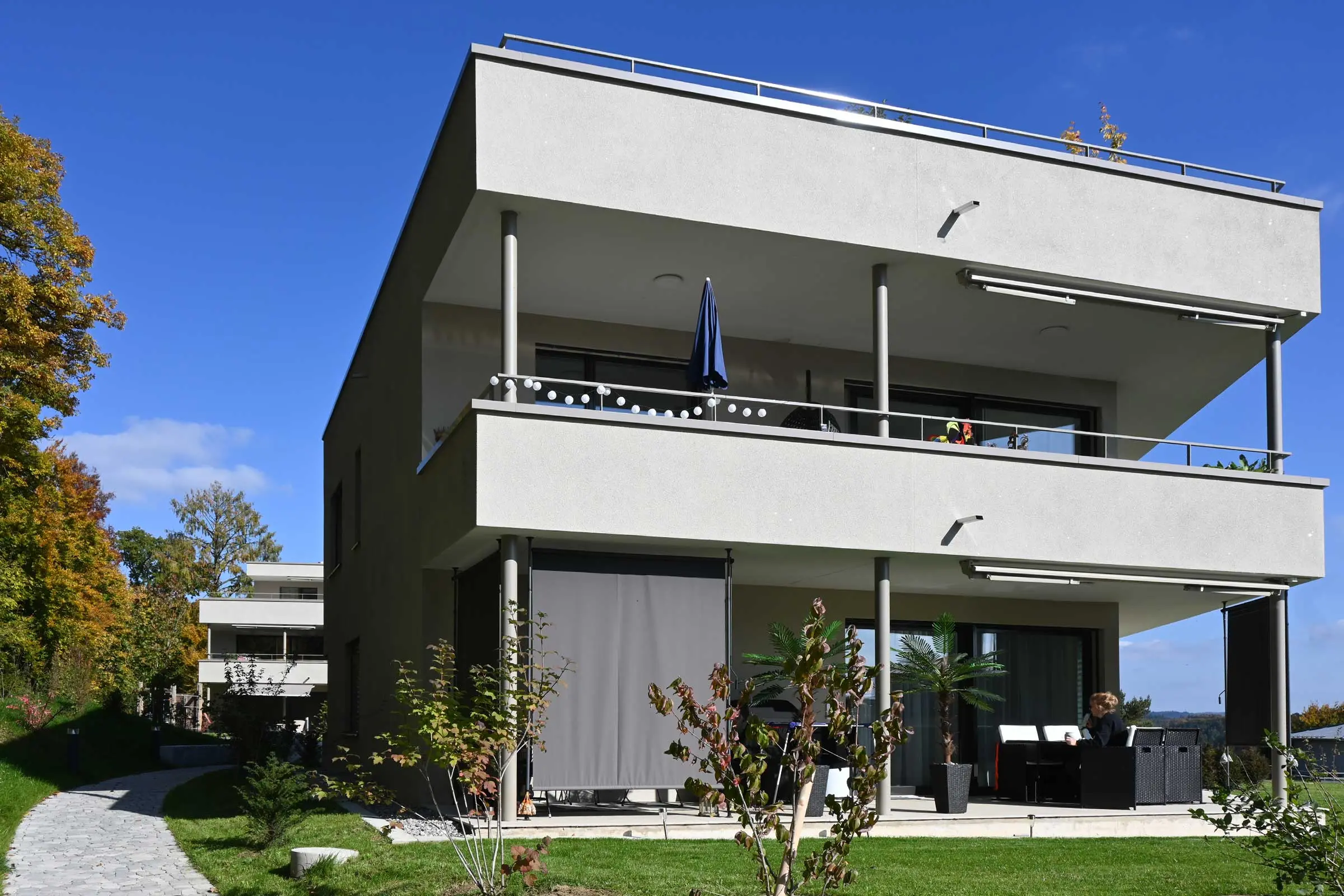 Frontansicht von Mehrfamilienhaus mit Balkon und Freisitz mit heller Putzfassade