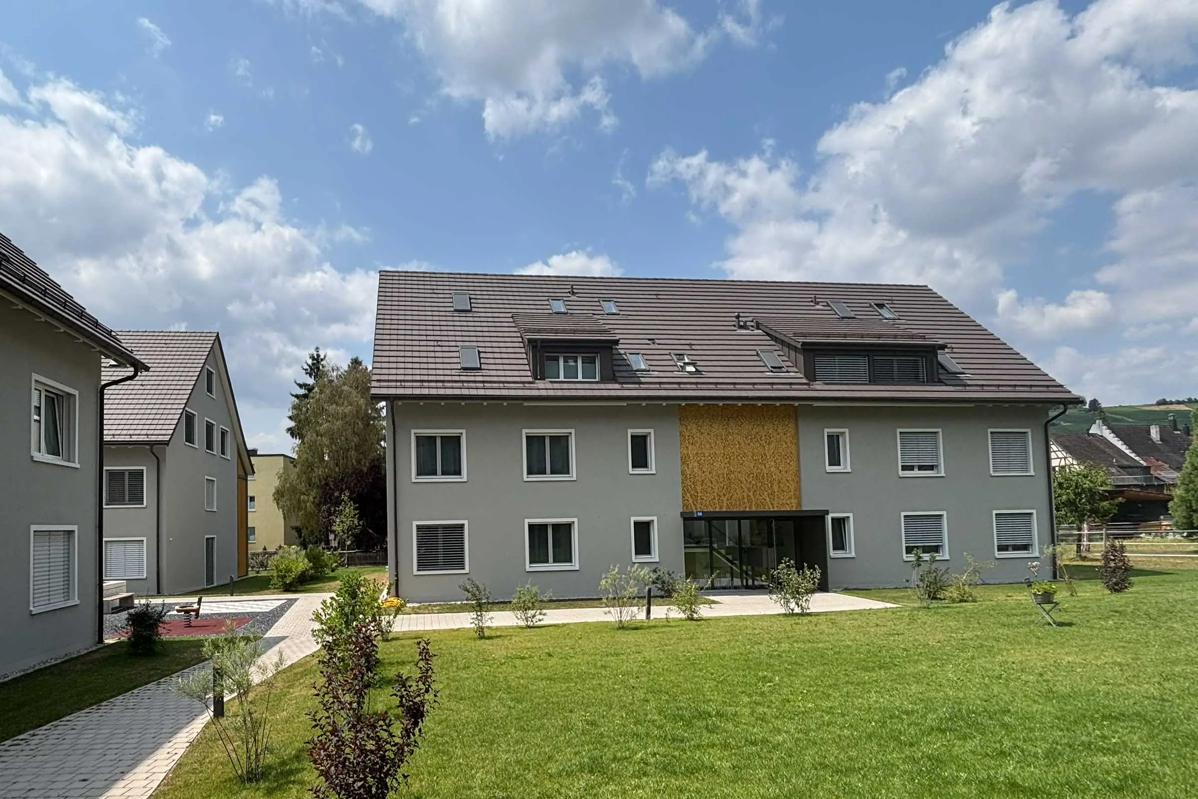 2 Mehrfamilienhäuser mit grauer Fassade und hellen Fensterumrandungen im rechten Winkel angeordnet