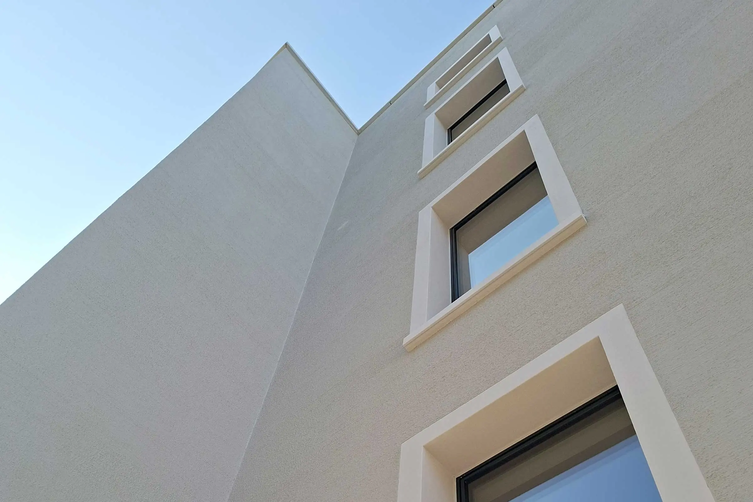 Mehrfamiienhaus mit hellem Putz und hellen Fensterumrandungen aus StoDecoelementen von unten