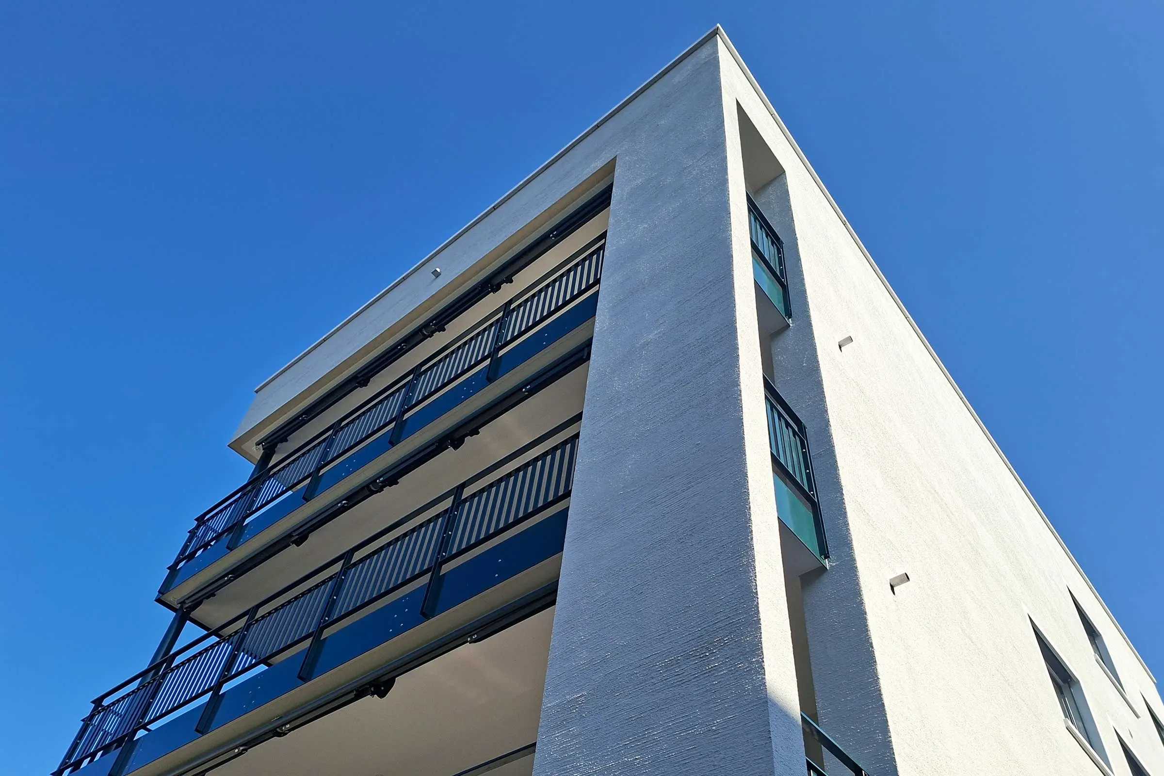 Ansicht einer Ecke von einem MFH mit hellem Putz mit Balkonen von unten