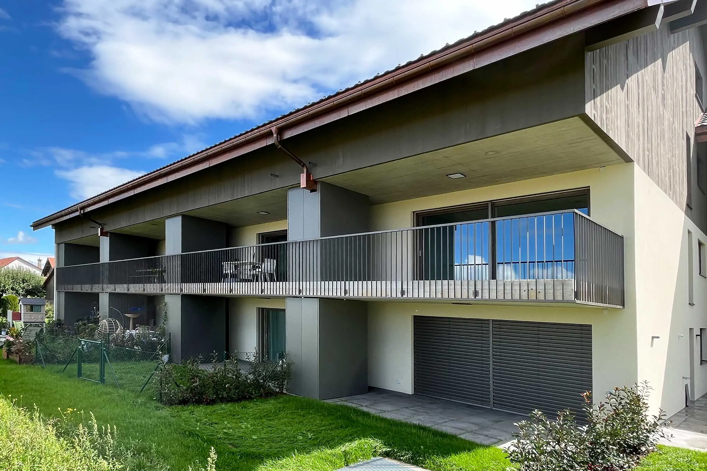 Immeuble collectif avec plusieurs balcons, façade en crépi clair et bardage en bois gris sur le toit