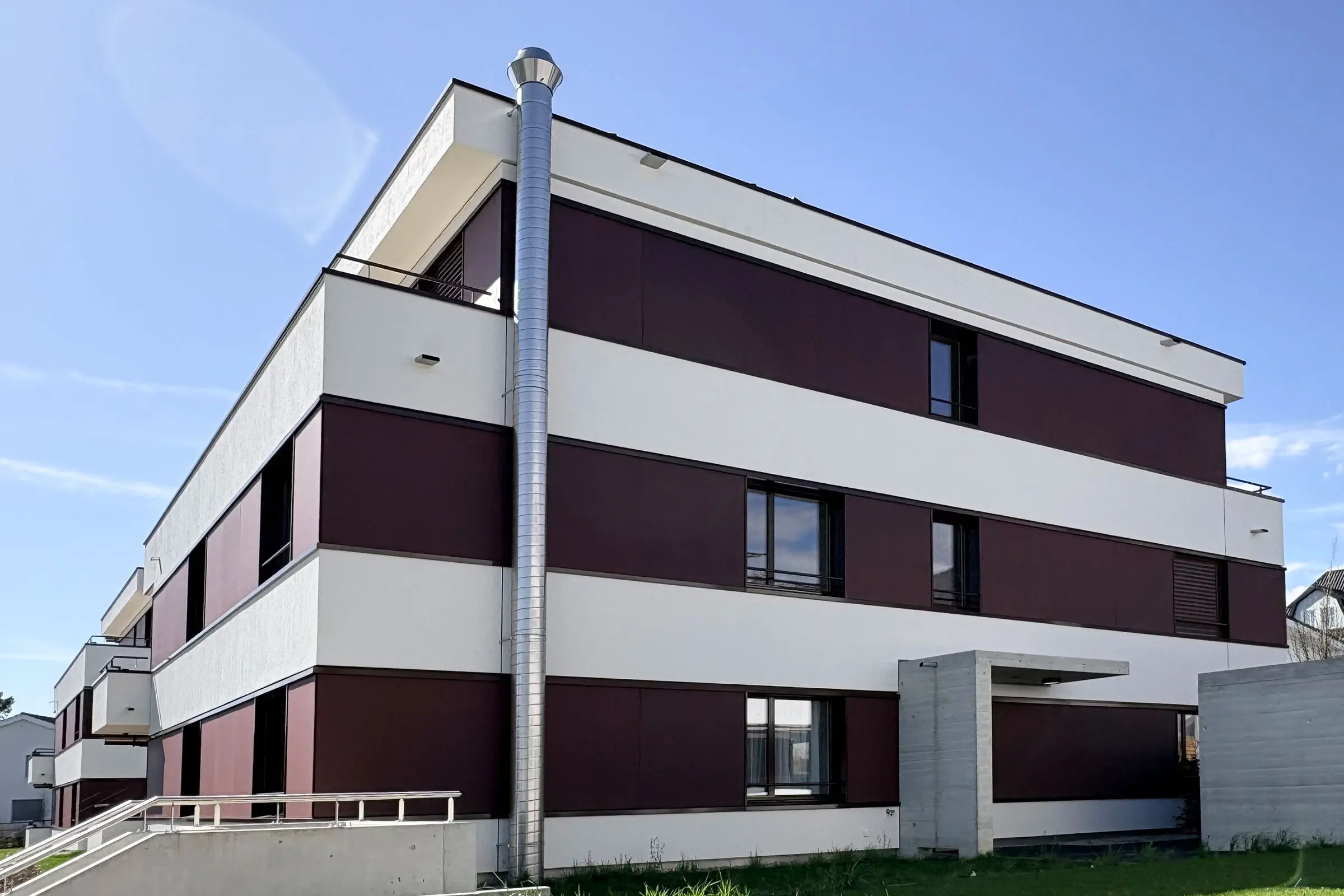 Mehrfamilienhaus mit einer Fassade aus roten Fassadenplatten und hellem Putz.