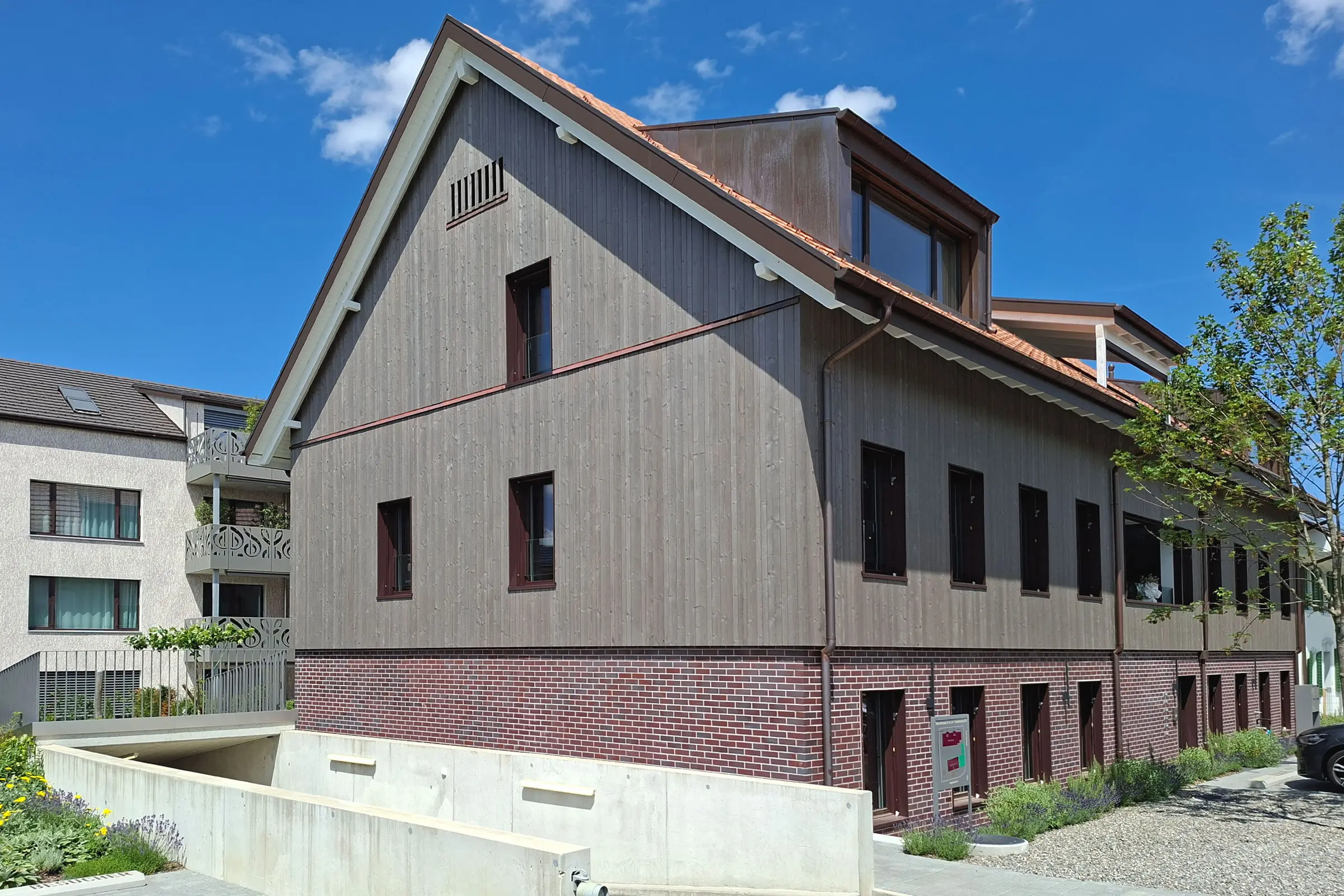 Mehrfamilienhaus mit Sockel aus rötlichem Klinker und grauer Holzfassade