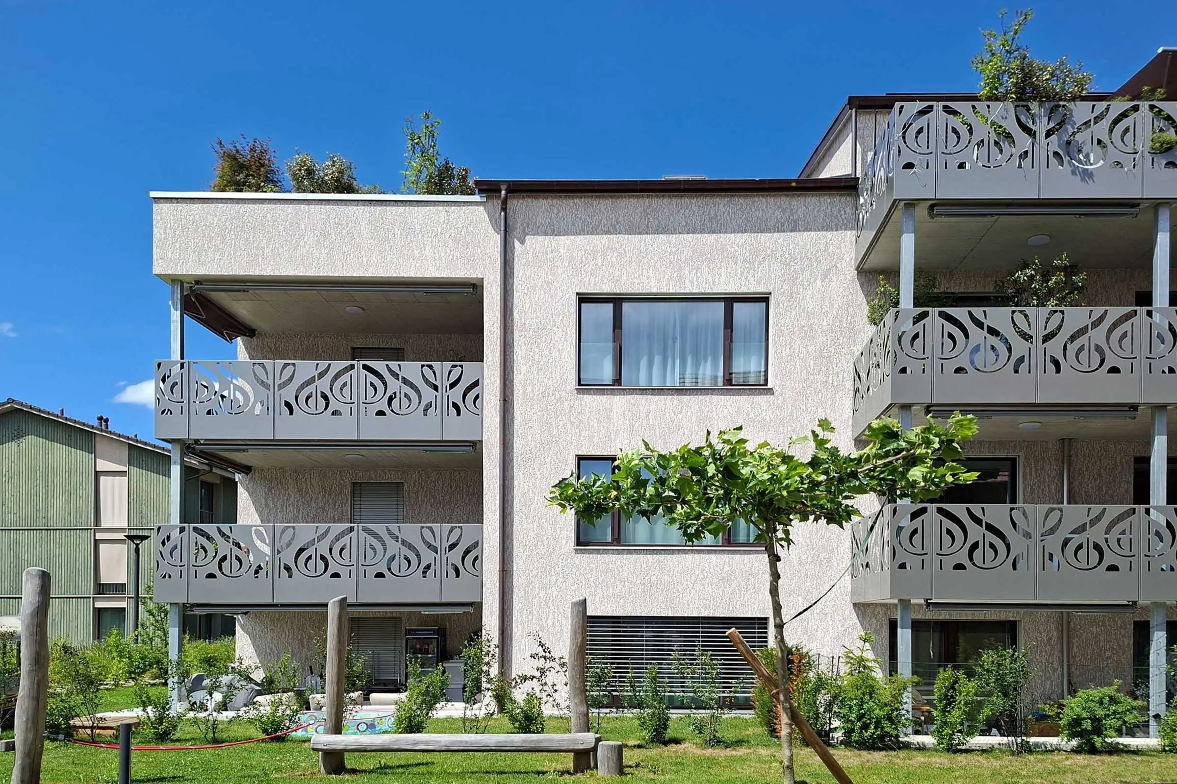 Mehrfamilienhaus mit beiger Putzfassade und grauen Balkonverkleidungen aus Metall