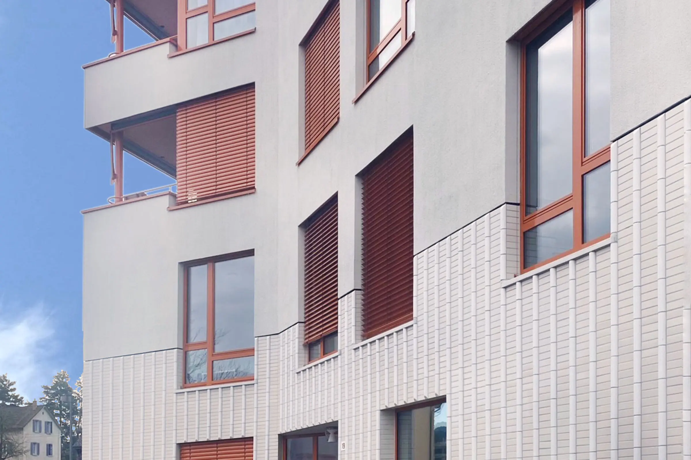 Ausschnitt von Mehrfamilienhaus mit grauer Fassade und einem Sockel aus weissem Vollstein