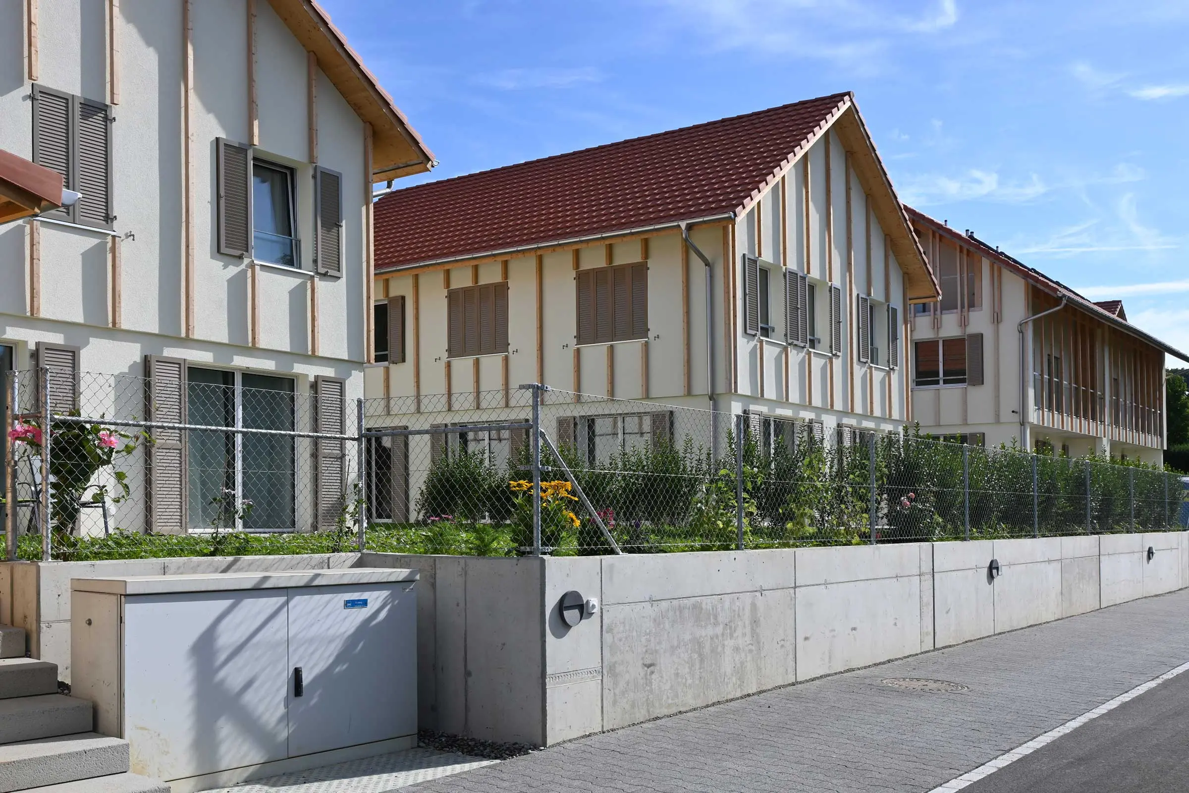 Wohnkomplex von der Strasse aus mit 3 Häusern mit Holzlatten auf heller Putzfassade