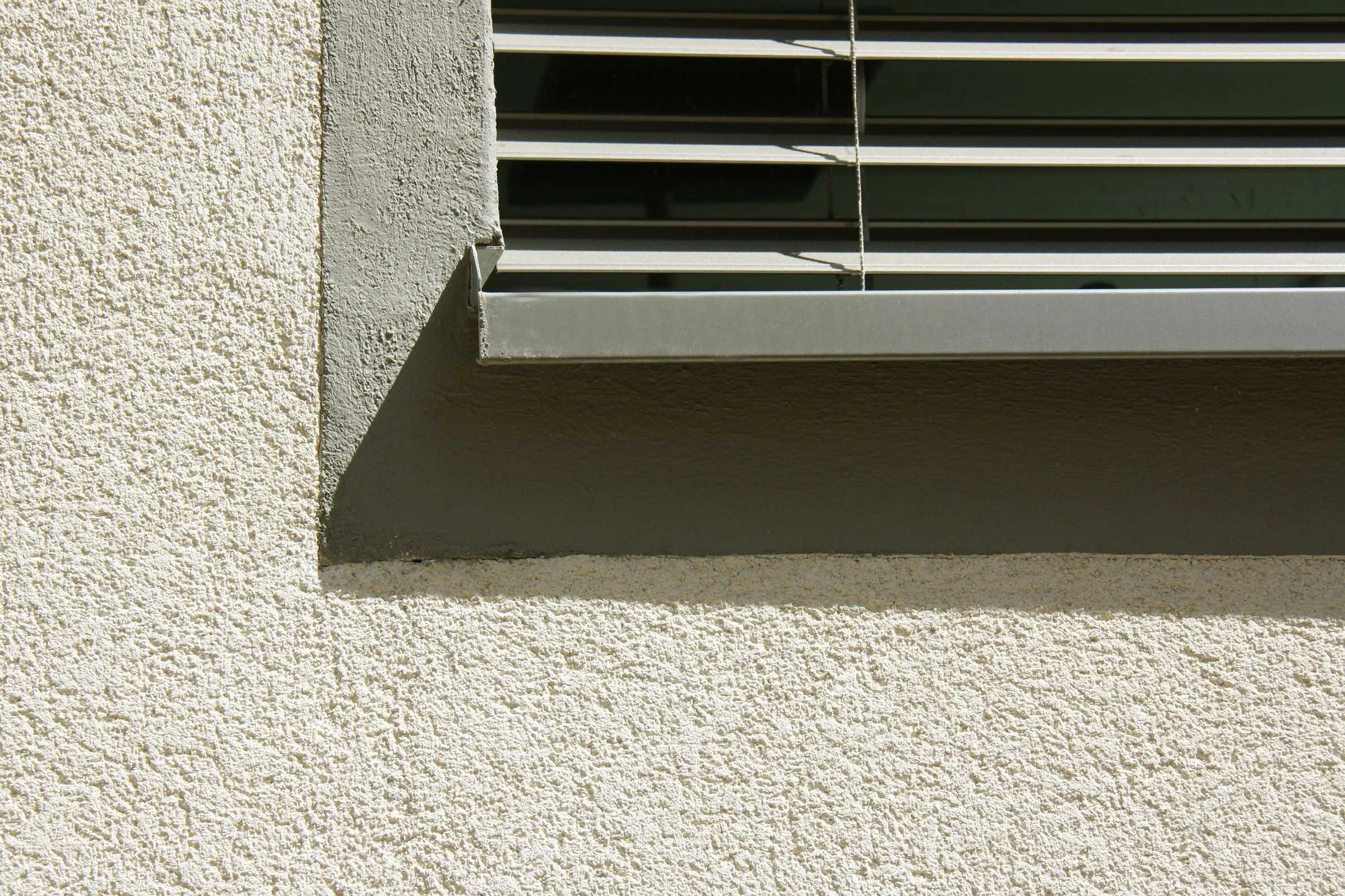 Gros plan sur une fenêtre avec un crépi clair et un encadrement de fenêtre gris