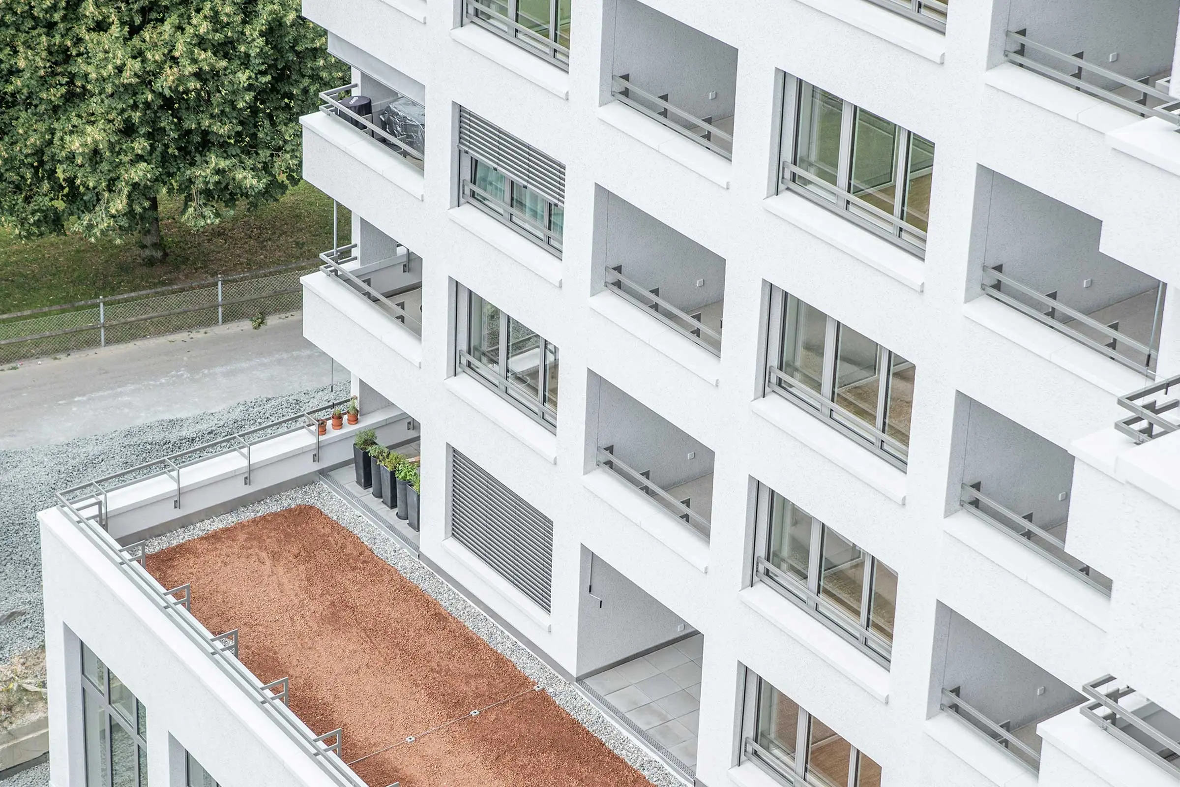 Sicht von oben auf mehrere Balkone einer Überbauung mit weisser Fassadenbeschichtung.
