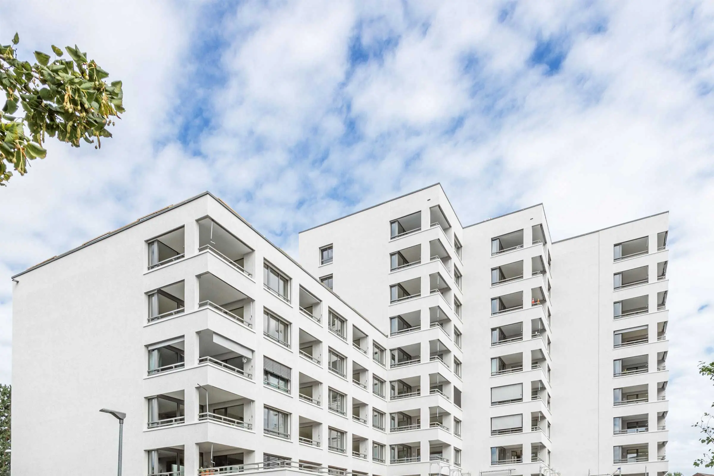 Gesamtansicht von vorne auf Überbauung mit mehreren Gebäuden mit weisser Fassadenbeschichtung.